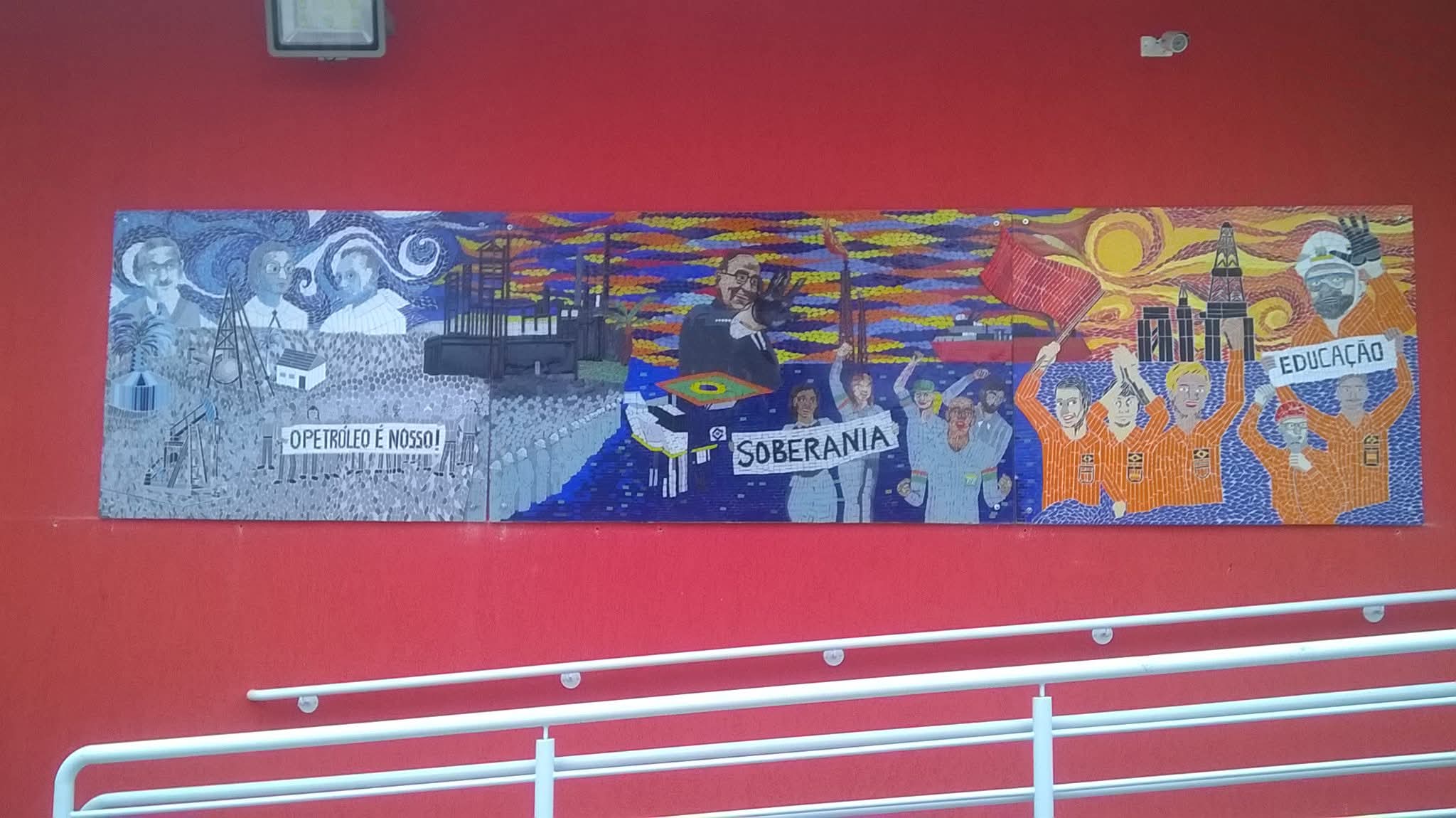 Painel mural em mosaico instalado sobre parede vermelha, do acervo aprovado do artista.