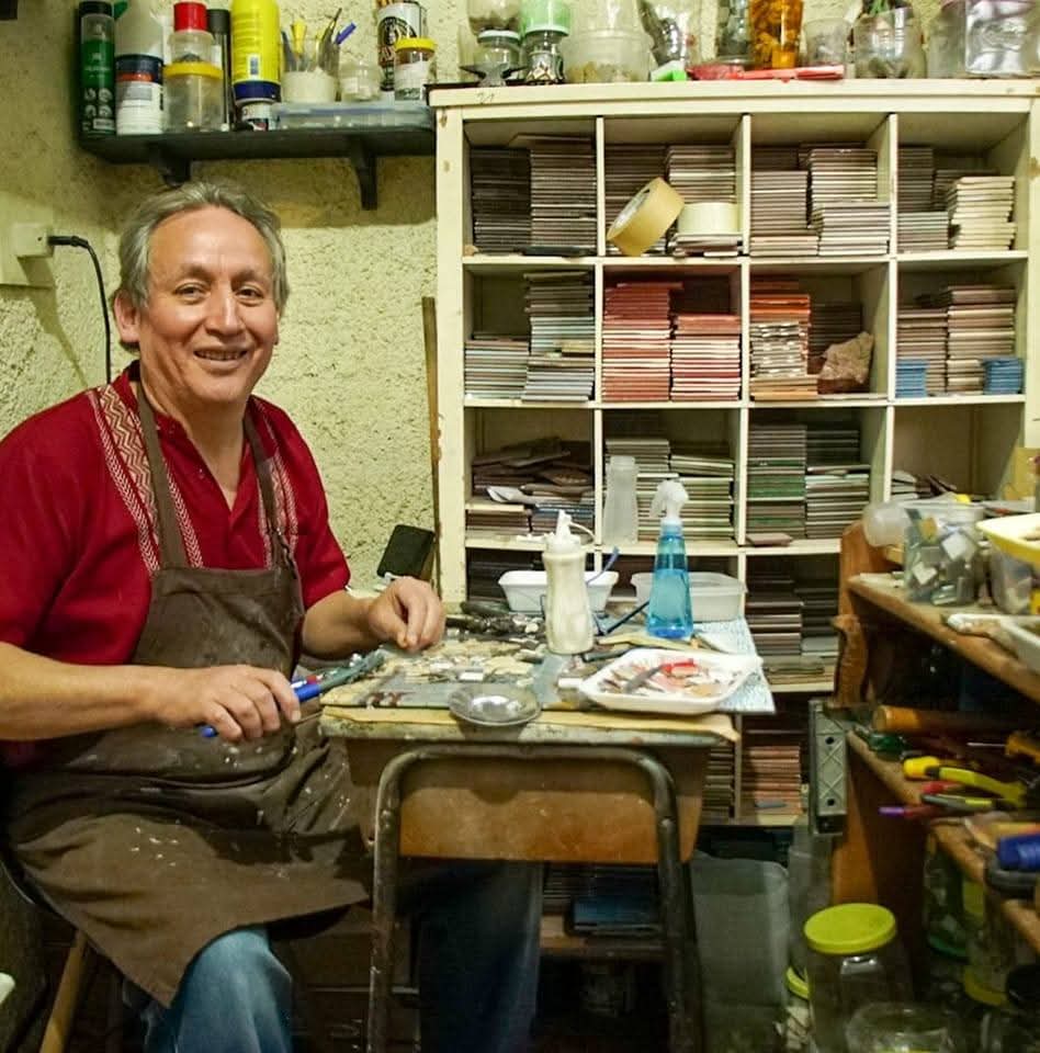 Javier Guerrero trabalhando no atelie diante de prateleiras com pastilhas e ferramentas.